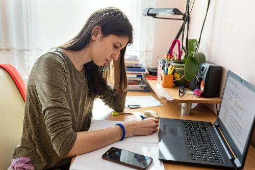 University age woman at a desk focussed on her work; with a notepad and laptop on her desk